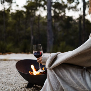 Woman enjoying red wine by outdoor fire pit overlooking forest at Bina Maya