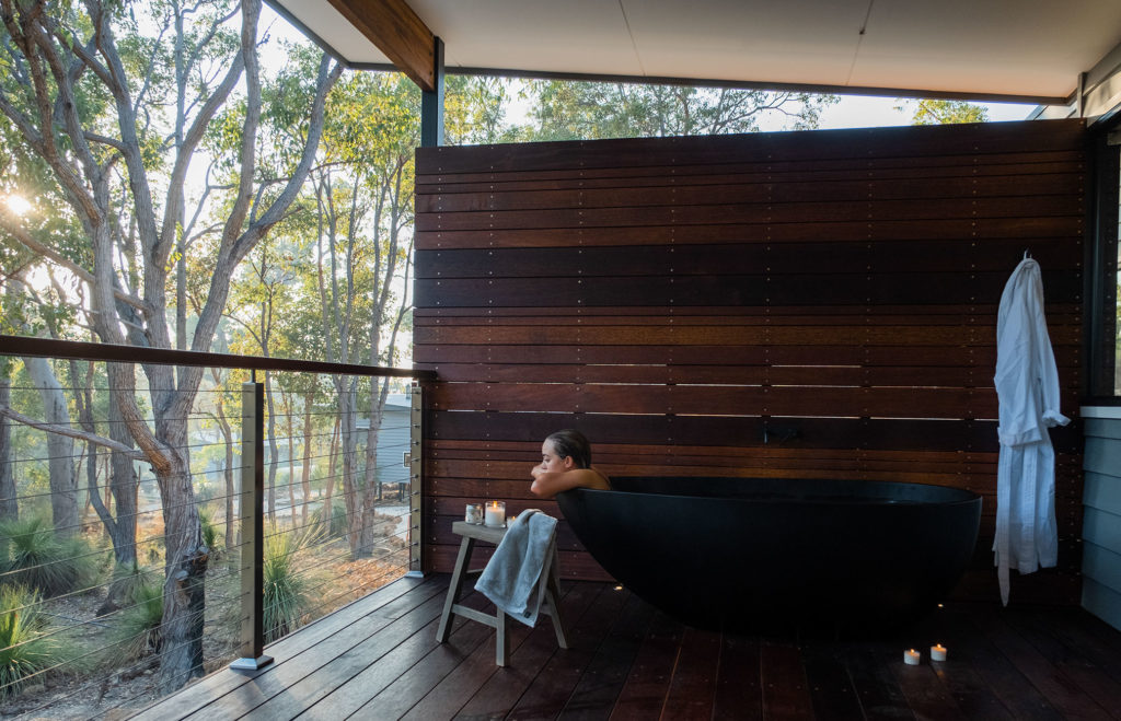 Woman taking bath in outdoor bath on balcony looking over forest