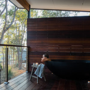 Woman taking bath in outdoor bath on balcony looking over forest